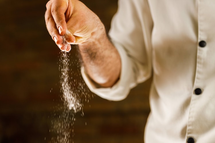 Person adding salt to their food.
